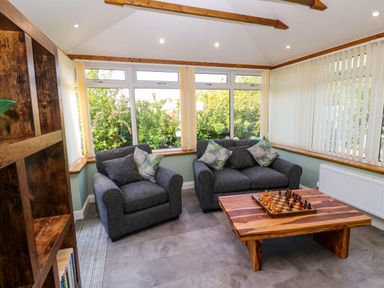 A sitting room with two gray armchairs a wooden coffee table with a chess set and large windows at Little Acorns in Gweek