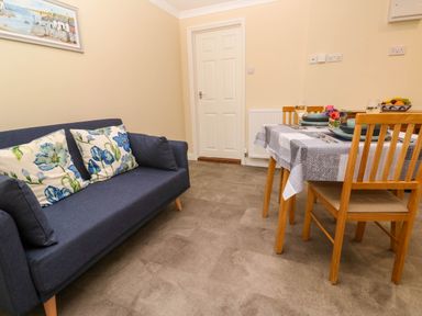 A living room with a blue sofa with floral cushions and a dining table with chairs and tableware at Little Acorns in Gweek