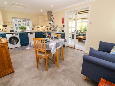 A kitchen with dark blue cabinets and a dining table set for two with wooden chairs at Little Acorns in Gweek