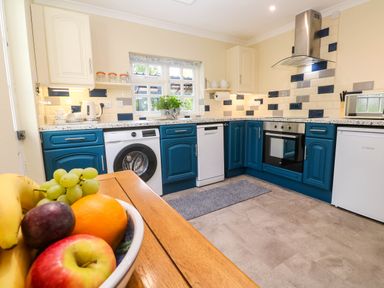 A kitchen with blue and white cabinets a washing machine dishwasher oven and a fruit bowl on a wooden table at Little Acorns in Gweek