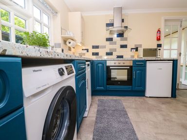 A kitchen with blue cabinets white appliances a washing machine oven microwave and a small fridge at Little Acorns in Gweek