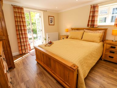 A bedroom with a wooden bed and nightstands with lamps and open doors leading outside at Little Acorns in Gweek