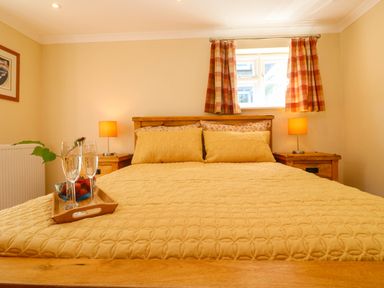 A bedroom with a wooden bed frame and yellow bedding with two bedside tables and lamps at Little Acorns in Gweek