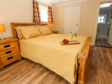 A bedroom with a wooden bed and bedside tables with lamps and a tray with strawberries and glasses on the bed at Little Acorns in Gweek