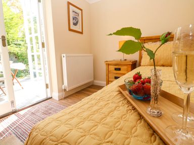 A bedroom with a bed covered by a yellow quilt and a wooden side table with a lamp at Little Acorns in Gweek