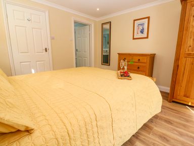 A bedroom with a yellow bedspread a wooden dresser a wooden wardrobe a wall mirror and two doors at Little Acorns in Gweek