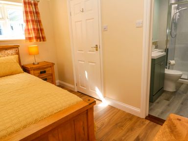 A bedroom with a wooden bed and bedside table with lamp next to a door leading to a bathroom at Little Acorns in Gweek