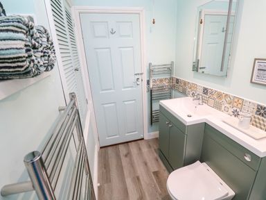 A bathroom with a toilet vanity mirror towel rack and patterned backsplash at Little Acorns in Gweek