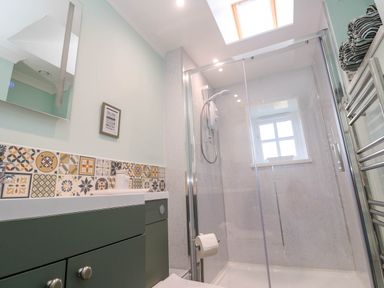 A bathroom with a green cabinet and patterned tiles a glass shower enclosure and a skylight at Little Acorns in Gweek