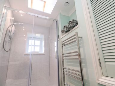 A bathroom with a glass shower enclosure a window a skylight a metal towel rack and striped towels on a shelf at Little Acorns in Gweek