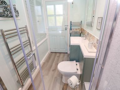 A bathroom with a toilet sink cabinet heated towel rail and shower at Little Acorns in Gweek