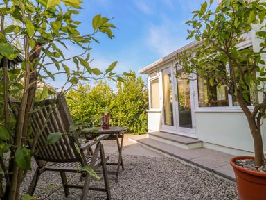 A small patio with a wooden table and chairs and plants outside a house at Little Acorns in Gweek