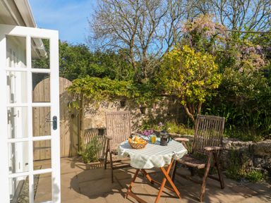 An outdoor patio with two wooden chairs and a table with a checkered tablecloth and breakfast items at Little Acorns in Gweek