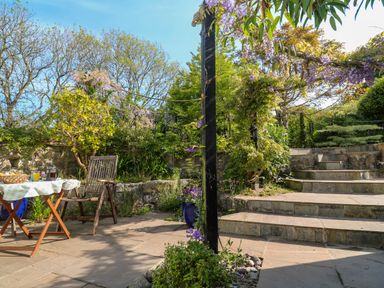 An outdoor patio area with a wooden chair and table set with food and drink surrounded by plants and stone steps at Little Acorns in Gweek