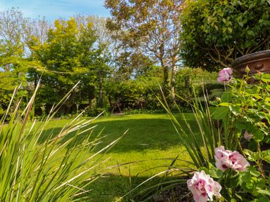 A garden with green grass flowers and a table with chairs at Little Acorns in Gweek