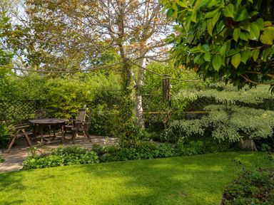 A garden with a wooden table and chairs under a tree surrounded by shrubs and greenery at Little Acorns in Gweek