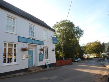 A street view of a building with a sign reading Black Swan and trees in the background at Little Acorns in Gweek