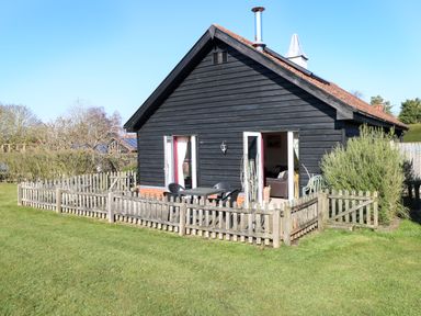 A small black wooden house with a red brick base and a wooden picket fence surrounding a patio area at Swallow Barn in Holton near Halesworth