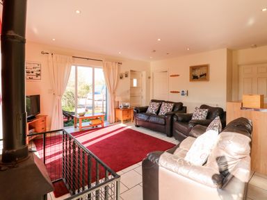 A living room with three leather sofas a red rug a wood stove and sliding glass doors at Swallow Barn in Holton near Halesworth