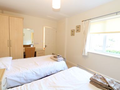 A bedroom with two single beds towels on beds a wardrobe a desk with chair and a window at Swallow Barn in Holton near Halesworth