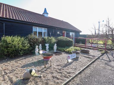 An exterior view of a building with a tiled roof and black wooden siding with garden statues bushes wheelbarrow and watering can in front at Swallow Barn Holton near Halesworth
