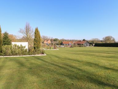 A large grassy garden with small trees and bushes and houses in the background at Swallow Barn in Holton near Halesworth