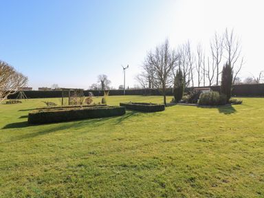 A large garden with trimmed hedges, trees, a picnic table, playground equipment, and a wind turbine at Swallow Barn Holton near Halesworth