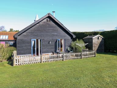 A fenced backyard with a wooden shed and black wooden house at Swallow Barn in Holton near Halesworth