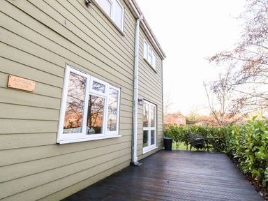 An exterior view of a house with beige siding a wooden deck and outdoor table and chairs at Arnside House in South Lakeland Leisure Village