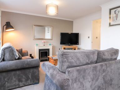 A living room with two grey sofas a fireplace a television on a wooden stand and a floor lamp at Arnside House in South Lakeland Leisure Village