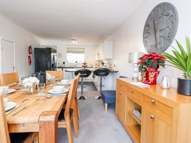 A dining area with a wooden table set for six and a sideboard with plants and decorations at Arnside House in South Lakeland Leisure Village