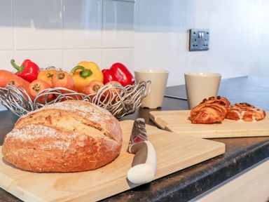 A kitchen counter with bread and a knife on a cutting board and a fruit basket with carrots and peppers at Arnside House in South Lakeland Leisure Village