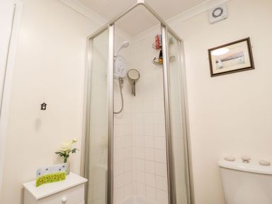 A bathroom with a corner shower enclosure a small cabinet with a vase and decorative item and a toilet with a framed picture on the wall at Arnside House in South Lakeland Leisure Village