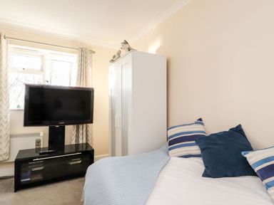A bedroom with a bed with pillows a wardrobe a television on a black stand and a window with curtains at Arnside House in South Lakeland Leisure Village