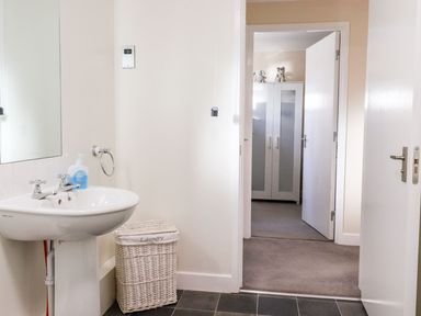 A bathroom with a sink and laundry basket opening to a room with a wardrobe at Arnside House in South Lakeland Leisure Village