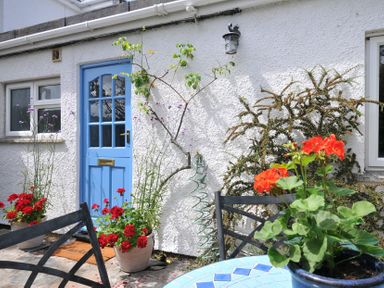 An outdoor area with a blue door, flower pots and a table at 2 Porthilly Cottages, Rock