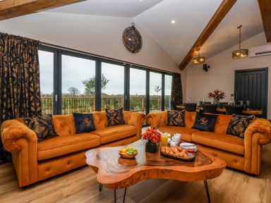 A living room with two orange sofas around a wooden coffee table and a dining table in the background at Routhorpe Lodge in Bainton near Great Driffield