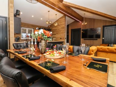 A dining table set with plates glasses cutlery and a floral centerpiece in a room with wood beams and a tv at Routhorpe Lodge in Bainton near Great Driffield