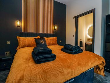 A bedroom with an orange bedspread and folded black towels on the bed at Routhorpe Lodge in Bainton near Great Driffield