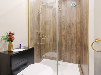 A bathroom with a glass shower enclosure wood panel walls a black cabinet with toiletries and flowers at Routhorpe Lodge in Bainton near Great Driffield