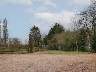 A gravel driveway with a wooden gate and trees on either side at Woodland Retreat Lodge in Brundish near Laxfield