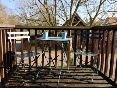 A wooden balcony with two metal chairs and a small round table with two mugs at Woodland Retreat Lodge Brundish near Laxfield