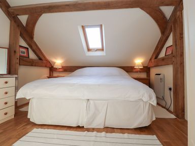 A bedroom with a large bed under a skylight and wooden beams at Woodland Retreat Lodge Brundish near Laxfield