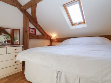 A bedroom with a bed under a skylight and a dresser with flowers and a mirror at Woodland Retreat Lodge in Brundish near Laxfield