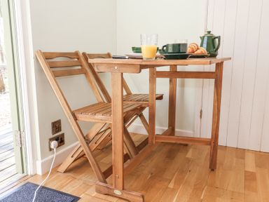A wooden table with two wooden folding chairs and breakfast items at Woodlands Retreat Shepherd's Hut Brundish near Laxfield