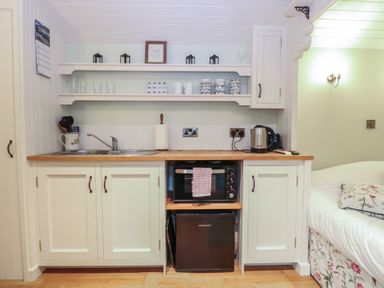 A kitchen area with sink, microwave, kettle, and shelves at Woodlands Retreat Shepherd's Hut Brundish near Laxfield