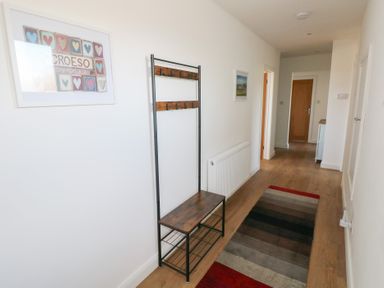 A hallway with a bench and coat rack a radiator a striped rug and framed pictures on the wall at Arfryn in Solva