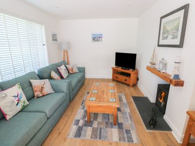 A living room with two green sofas wooden coffee table and a TV by a fireplace at Arfryn in Solva