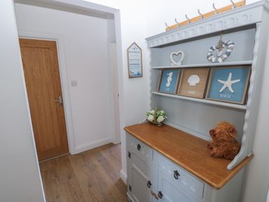 A hallway with a wooden door and a cabinet with decorative beach-themed items at Arfryn in Solva