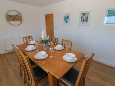 A dining room with a wooden table set with white dishes and glasses and wooden chairs at Arfryn in Solva